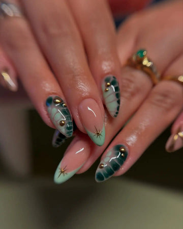 Handmade press-on nails with green gradient, floral patterns, and gold accents on natural nails.
