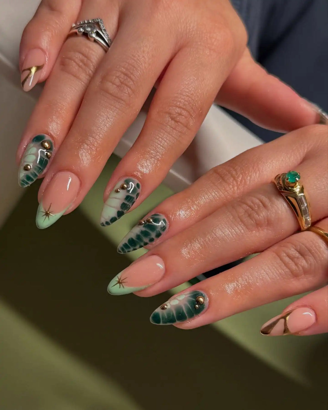 Handmade press-on nails with green gradient, floral patterns, and gold accents on natural nails.