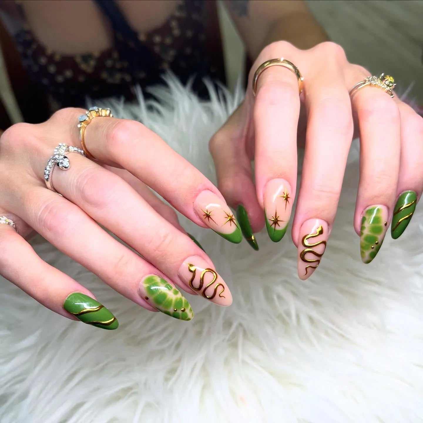 Hand with handmade forest green press-on nails featuring gold snake, star, and celestial designs