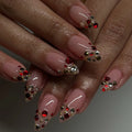Hand with almond-shaped press-on nails featuring ruby red, gold, and clear crystal accents