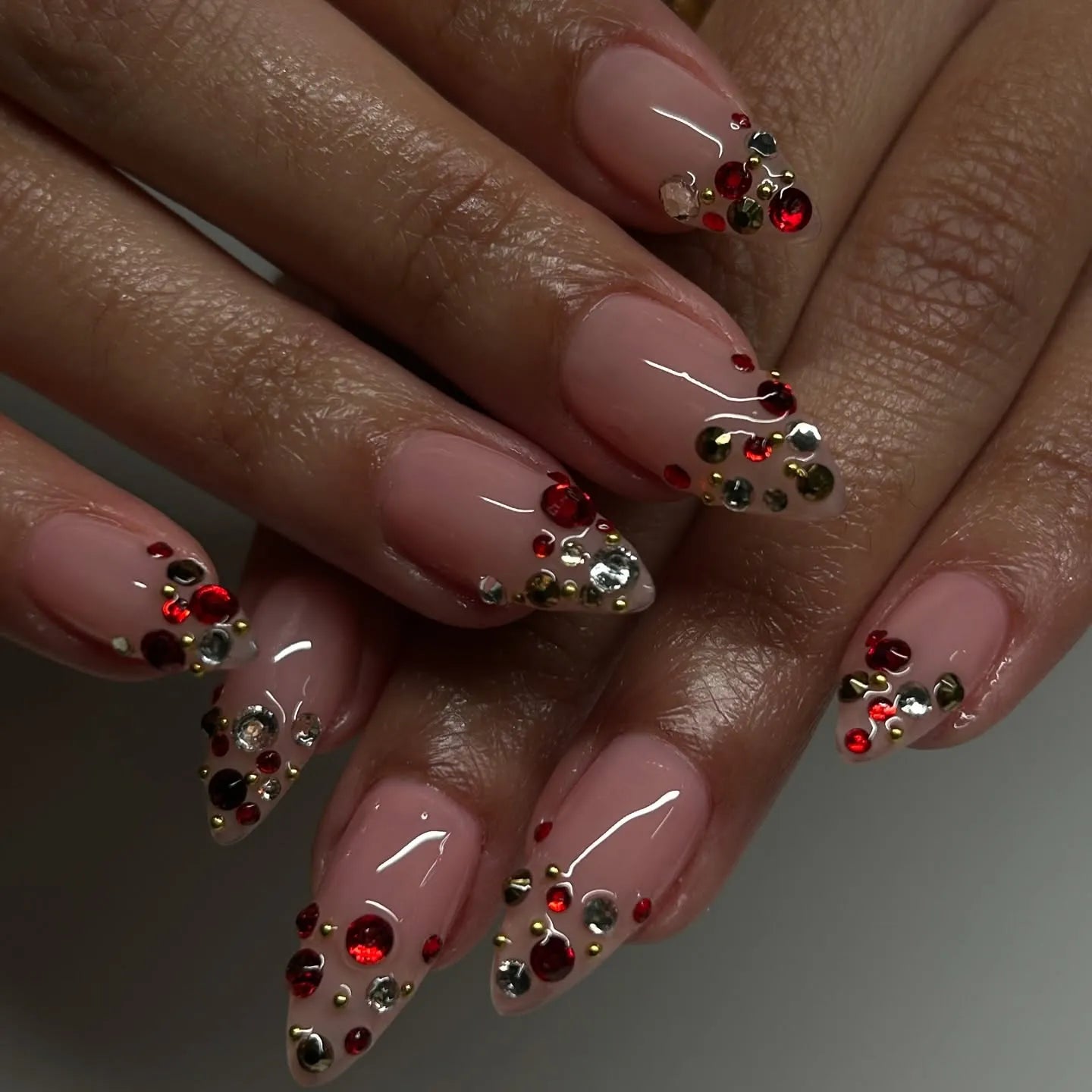Hand with almond-shaped press-on nails featuring ruby red, gold, and clear crystal accents