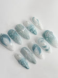 Handmade blue and white press-on nails with glittery seafoam, starfish, and shell ocean details.