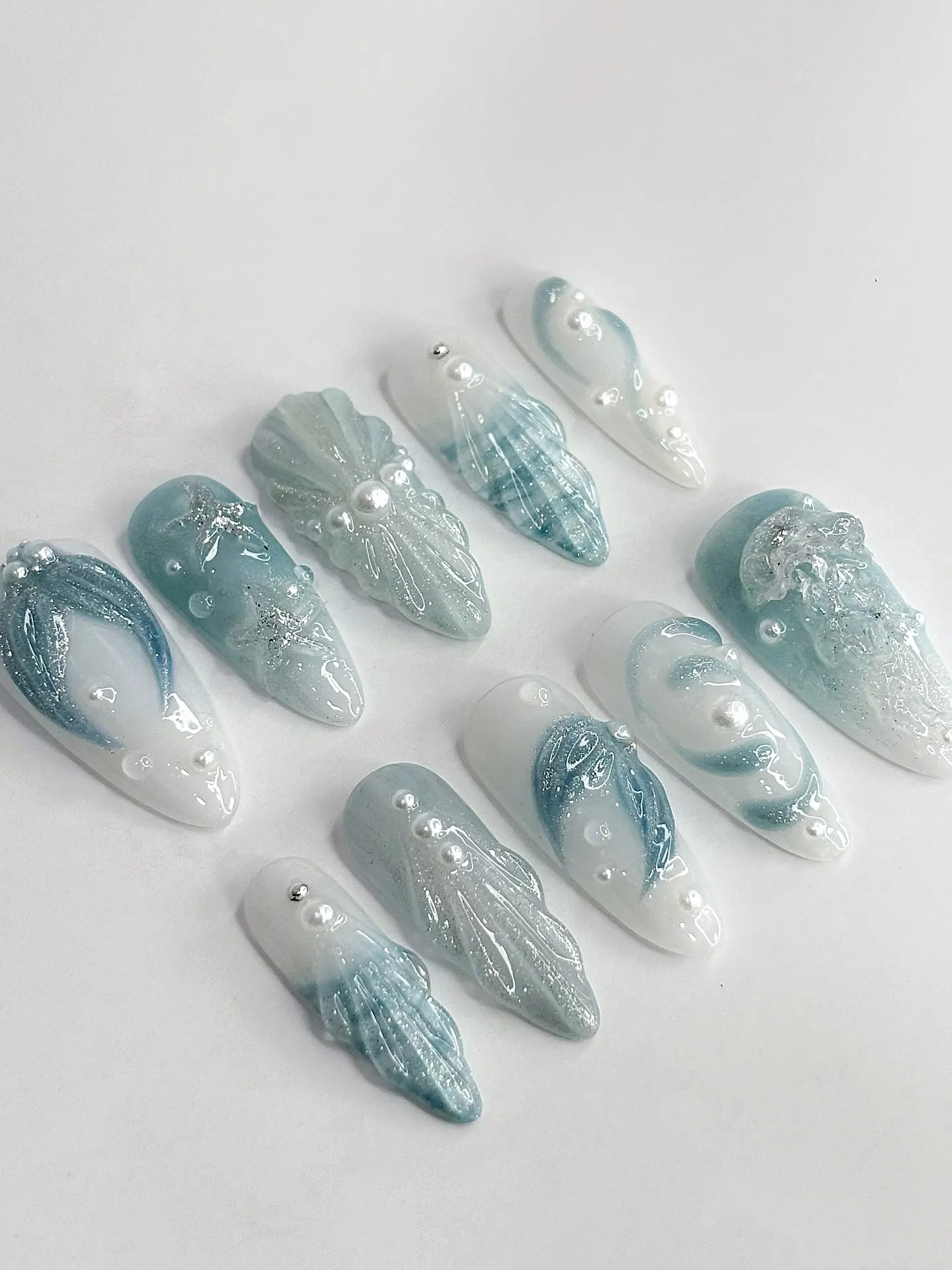 Handmade blue and white press-on nails with glittery seafoam, starfish, and shell ocean details.