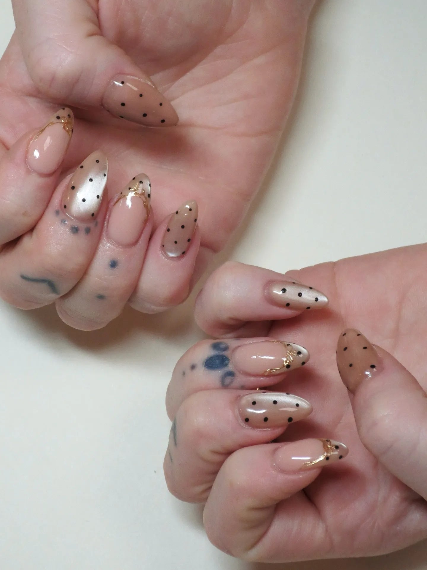 Hand with almond-shaped press-on nails, nude and pearlescent tones, gold filigree, black polka dots