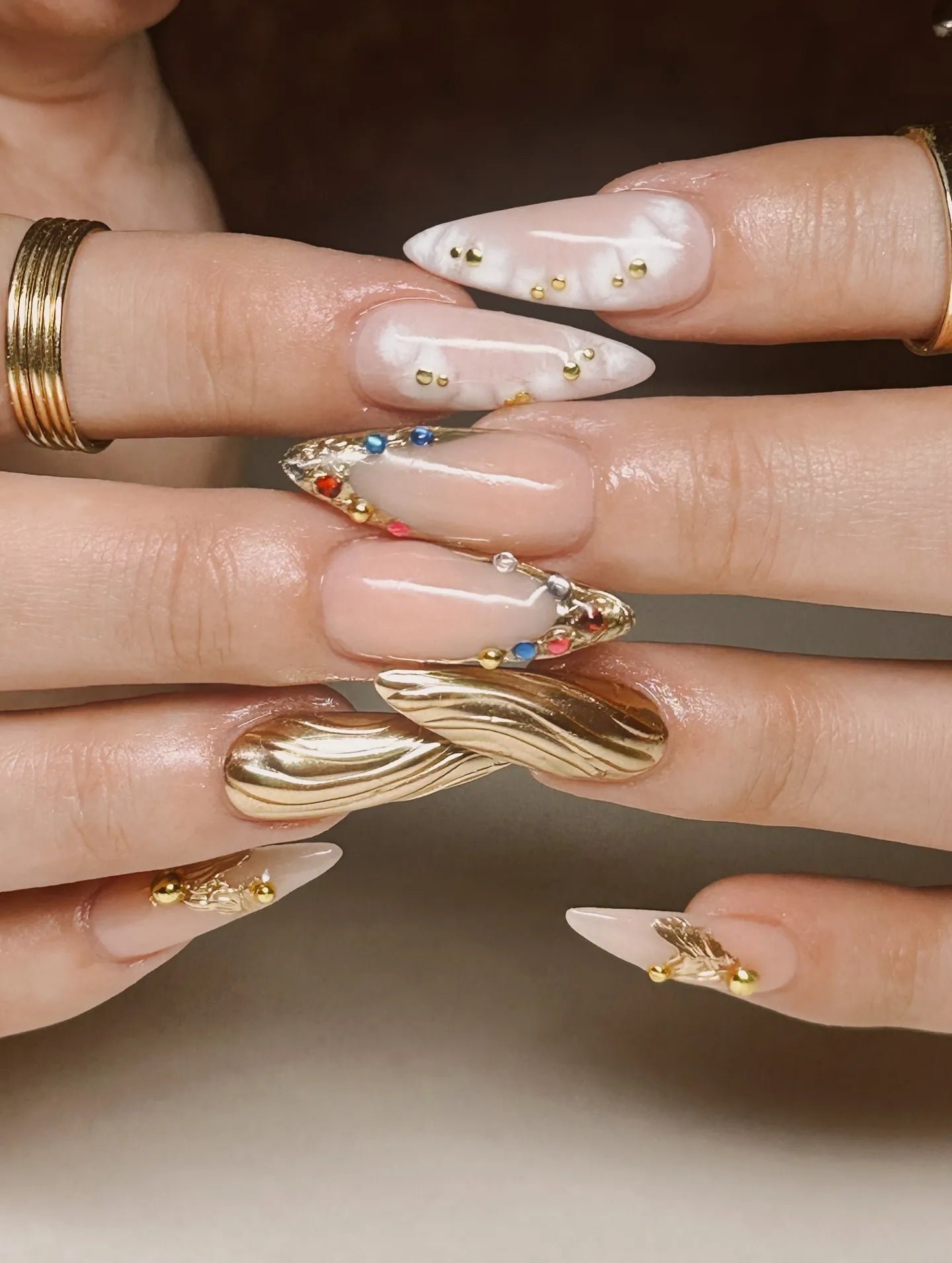 Handmade press-on nails with gold wavy chrome, marble accents, and multicolor gemstones.