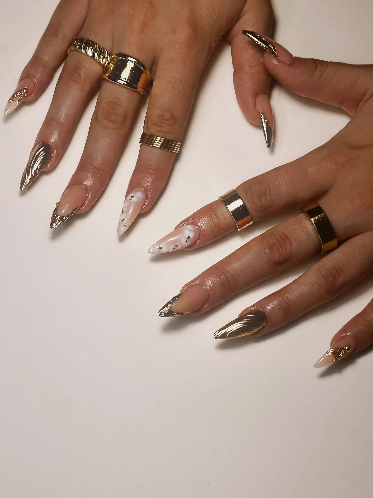 Hand with handmade stiletto press-on nails featuring gold chrome, marble, and gemstone accents.