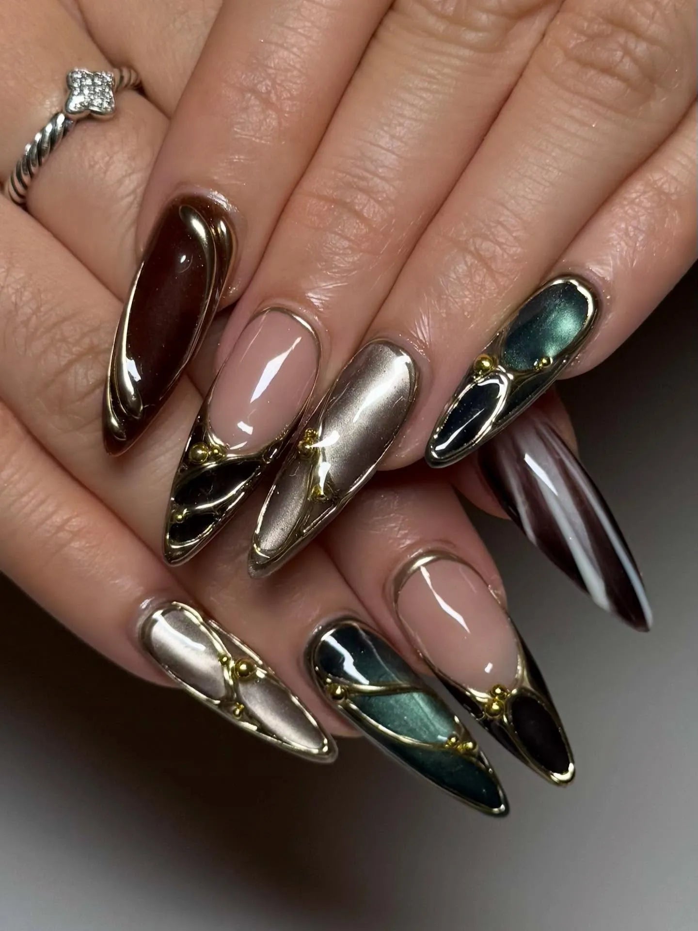 Handmade stiletto press-on nails with metallic jewel tones, chrome accents, and gold details