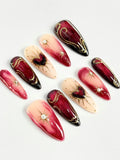 Handmade crimson ombre press-on nails with golden heart and starburst designs.