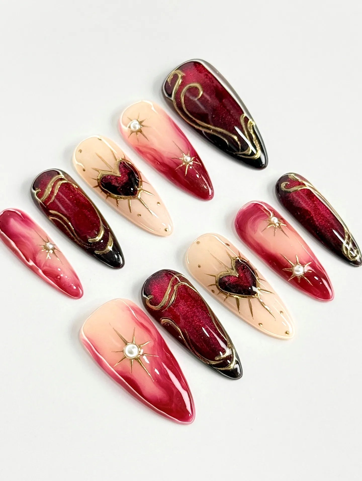 Handmade crimson ombre press-on nails with golden heart and starburst designs.