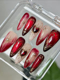 Handmade red ombre press-on nails with gold heart, starburst, and pearl accents in a case.