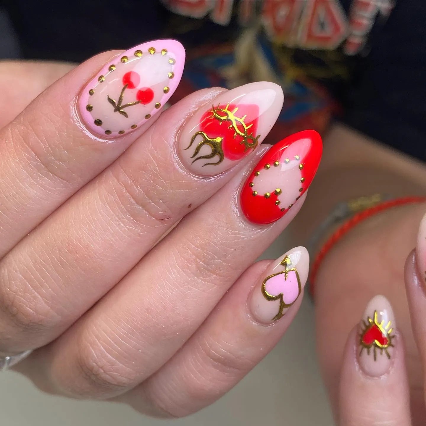 Hand with handmade press-on nails featuring red hearts, cherries, gold accents, and gothic designs.
