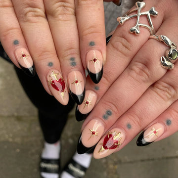 Handmade press-on nails with black French tips, gold stars, and red heart accents.