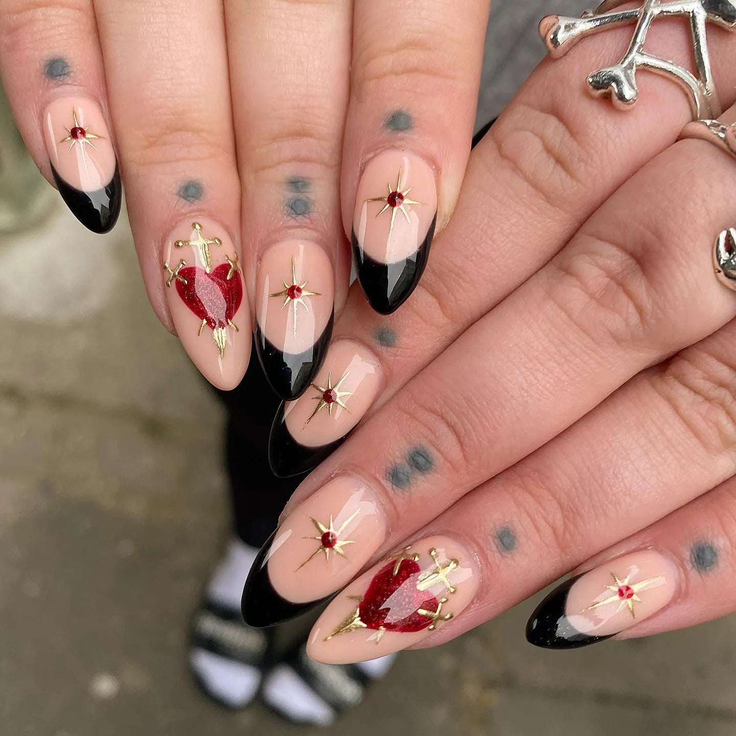 Hand with handmade press-on nails featuring black French tips, sacred heart and star designs.