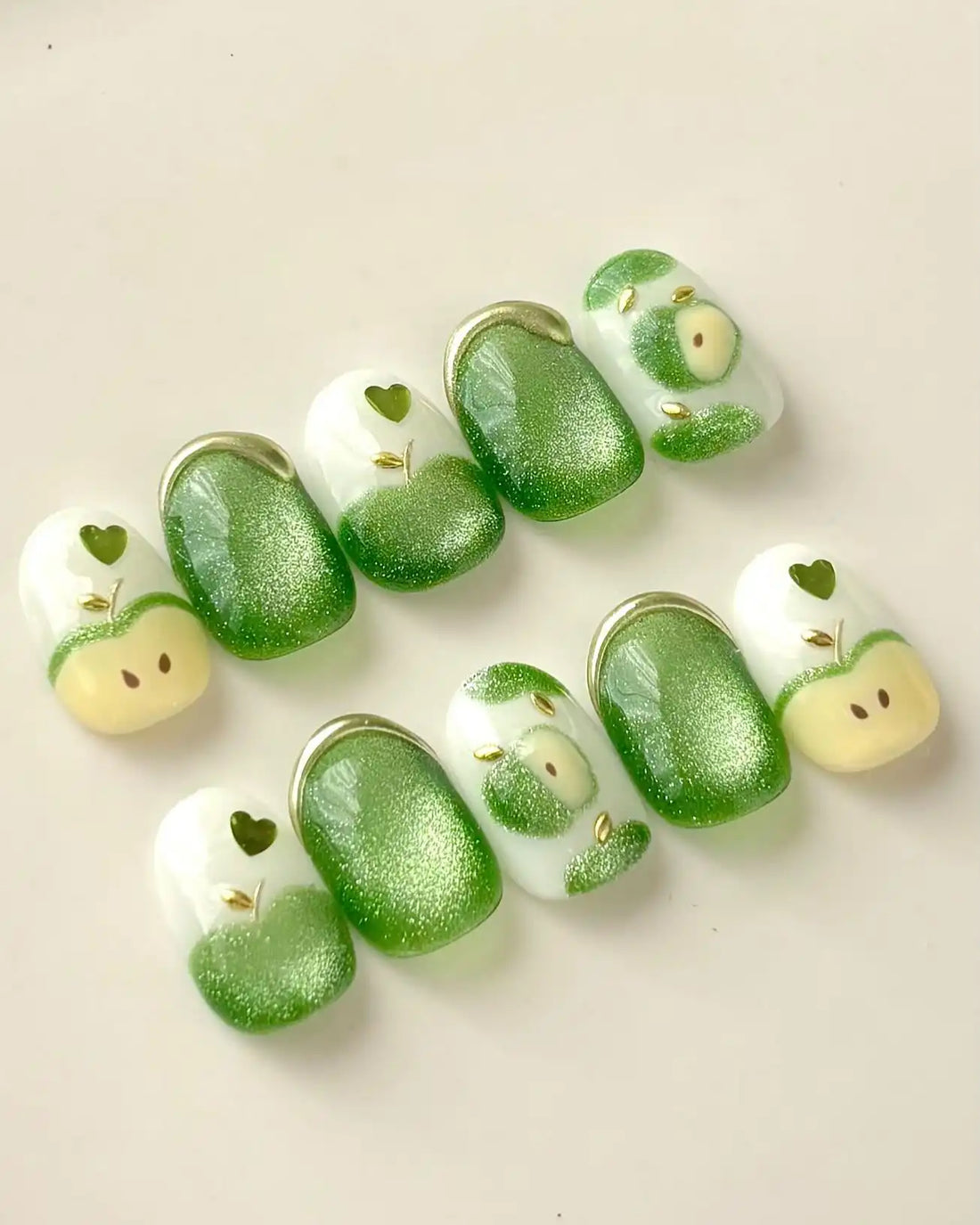 Handmade press-on nails with green apple cat eye shimmer and heart design on white base.