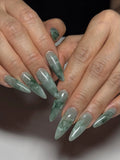 Hand with extra long stiletto press-on nails in green jade marble stone effect