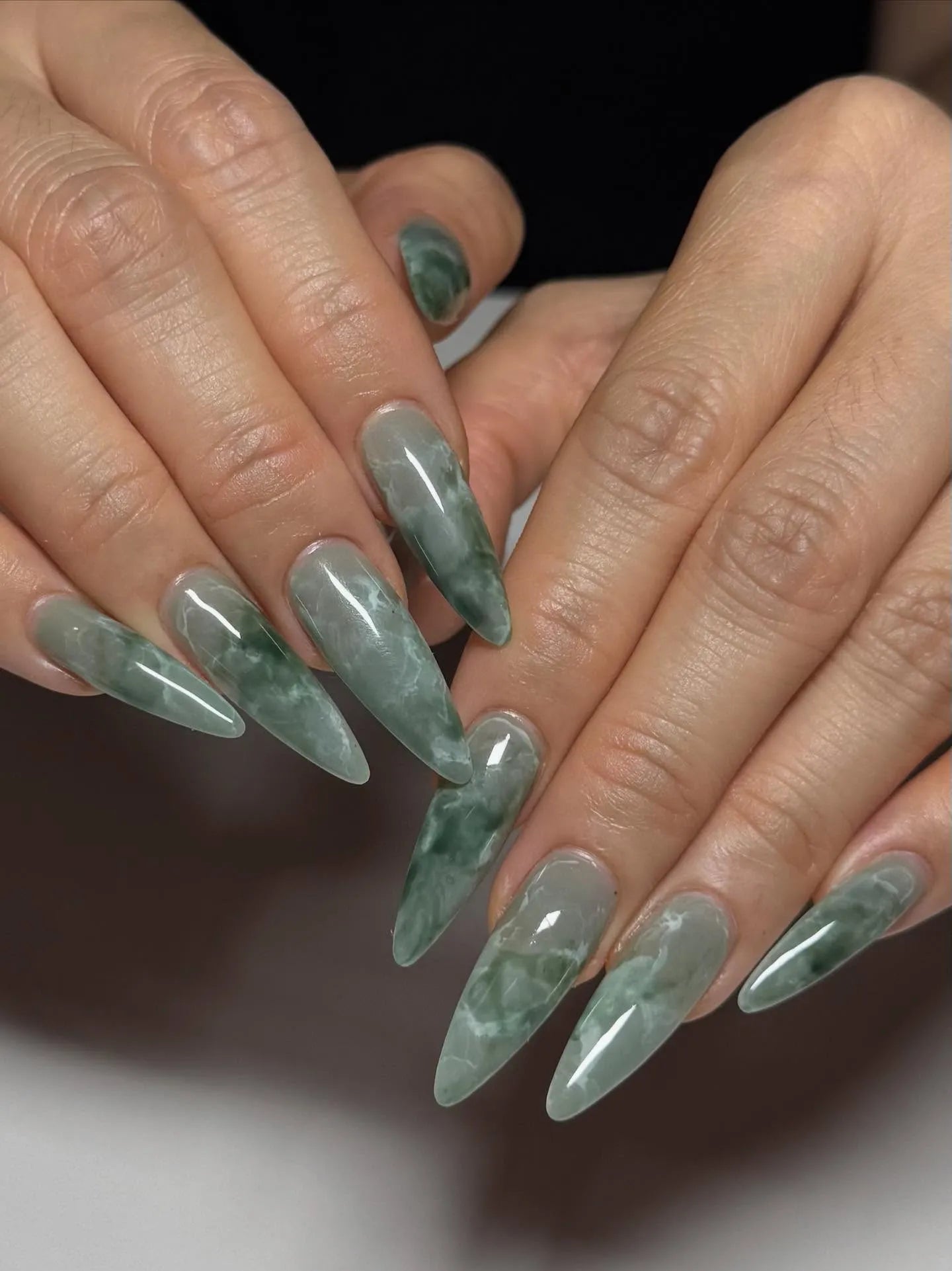 Hand with extra long stiletto press-on nails in green jade marble stone effect