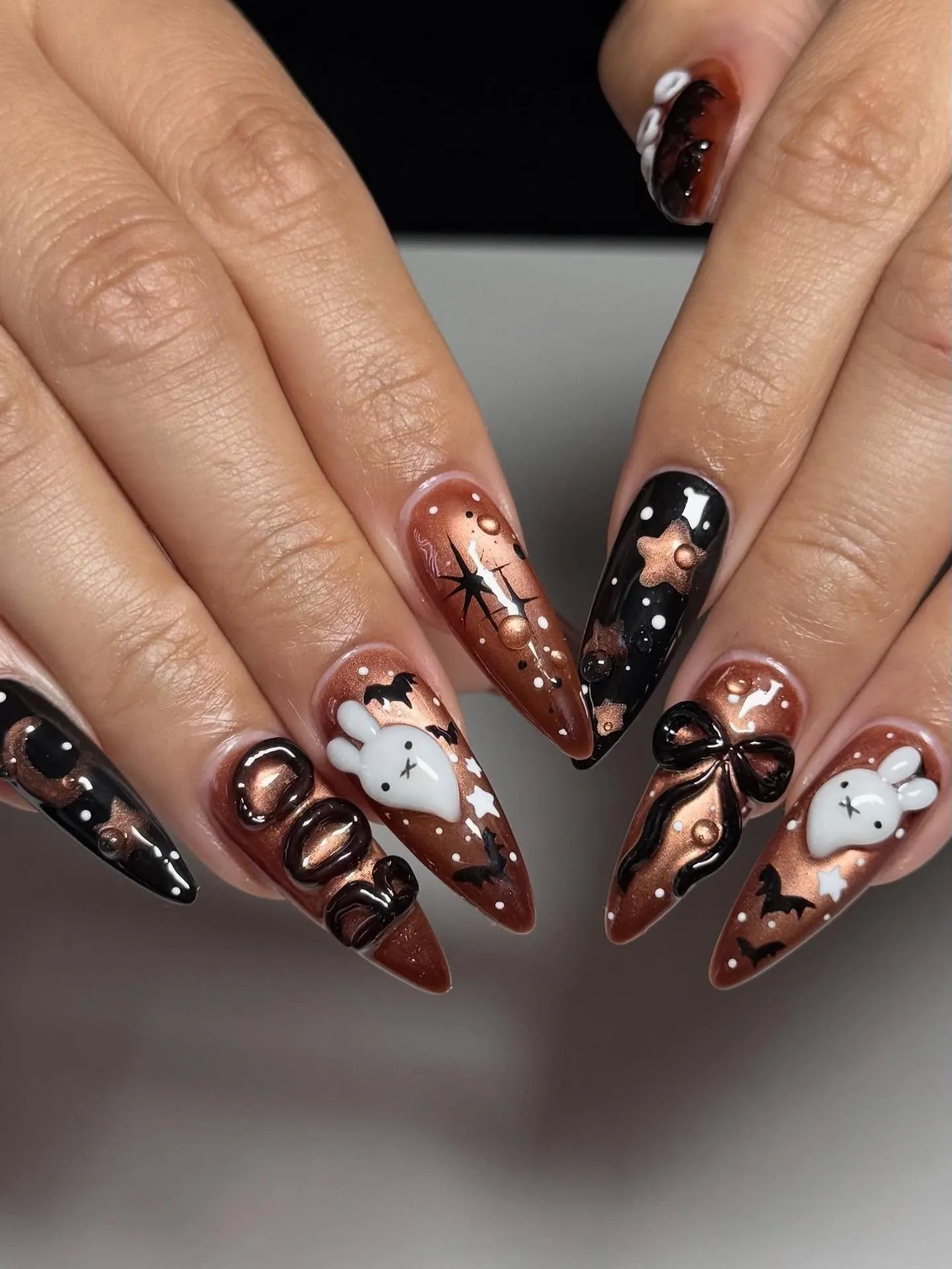 Handmade Halloween press-on nails with metallic bronze and black ghost, bat, and bow designs.