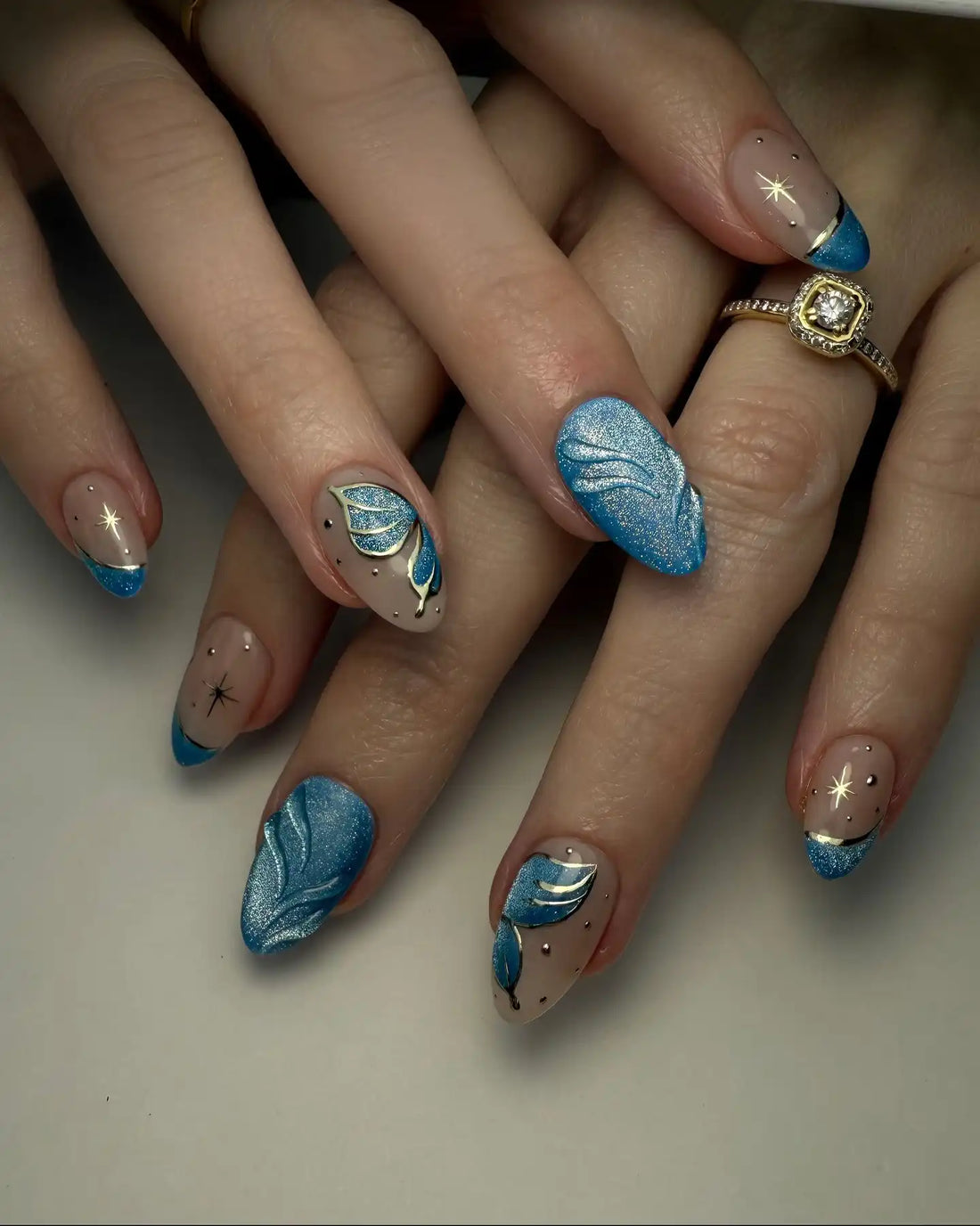 Handmade press-on nails with iridescent blue butterfly wing designs and gold star accents.