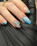 Hand with handmade press-on nails featuring iridescent blue butterfly wing and gold star accents