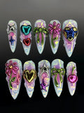 Handmade iridescent press-on nails with 3D metallic hearts, stars, bows, flowers, and cherries