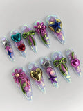 Handmade iridescent press-on nails with 3D metallic bows, hearts, stars, and floral designs.