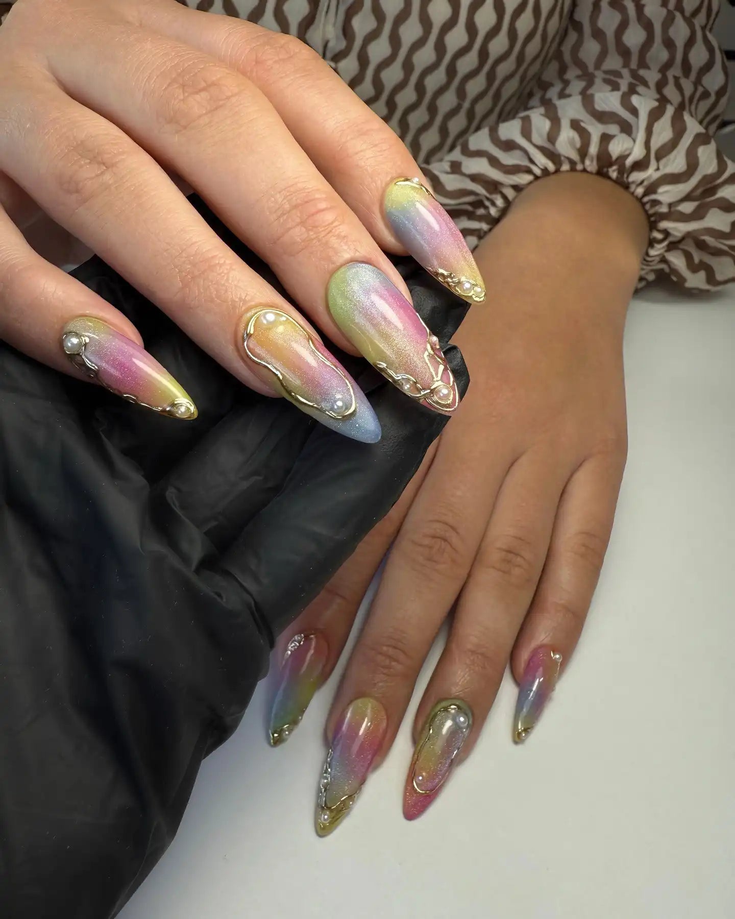 Hand with long iridescent pastel press-on nails, gold accents and pearl 3D details