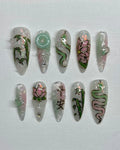Handmade iridescent pink and jade green press-on nails with lotus, bamboo, and snake designs.