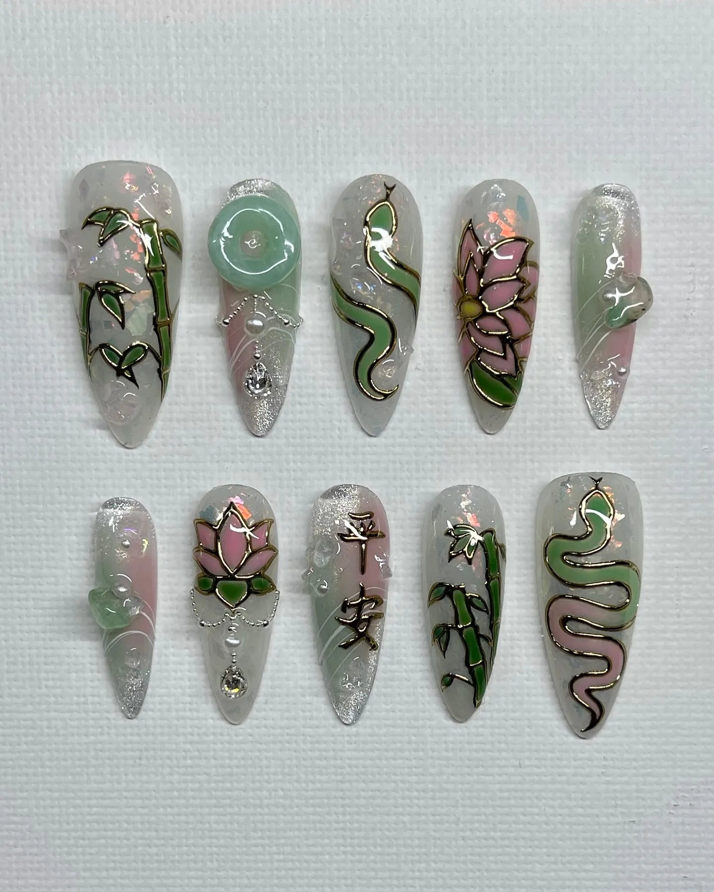 Handmade iridescent pink and jade green press-on nails with lotus, bamboo, and snake designs.