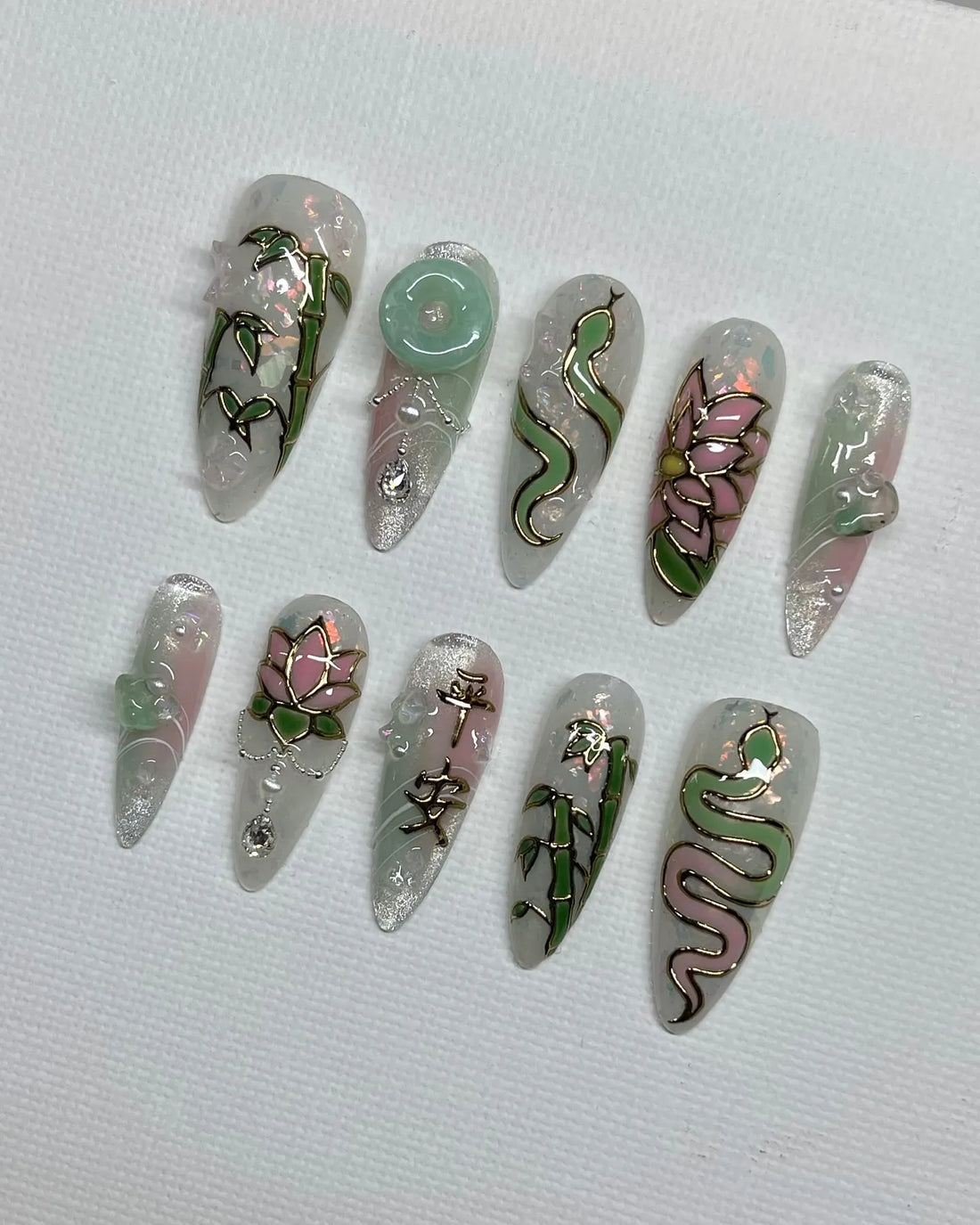 Handmade iridescent pink and jade green press-on nails with lotus, bamboo, and snake designs.