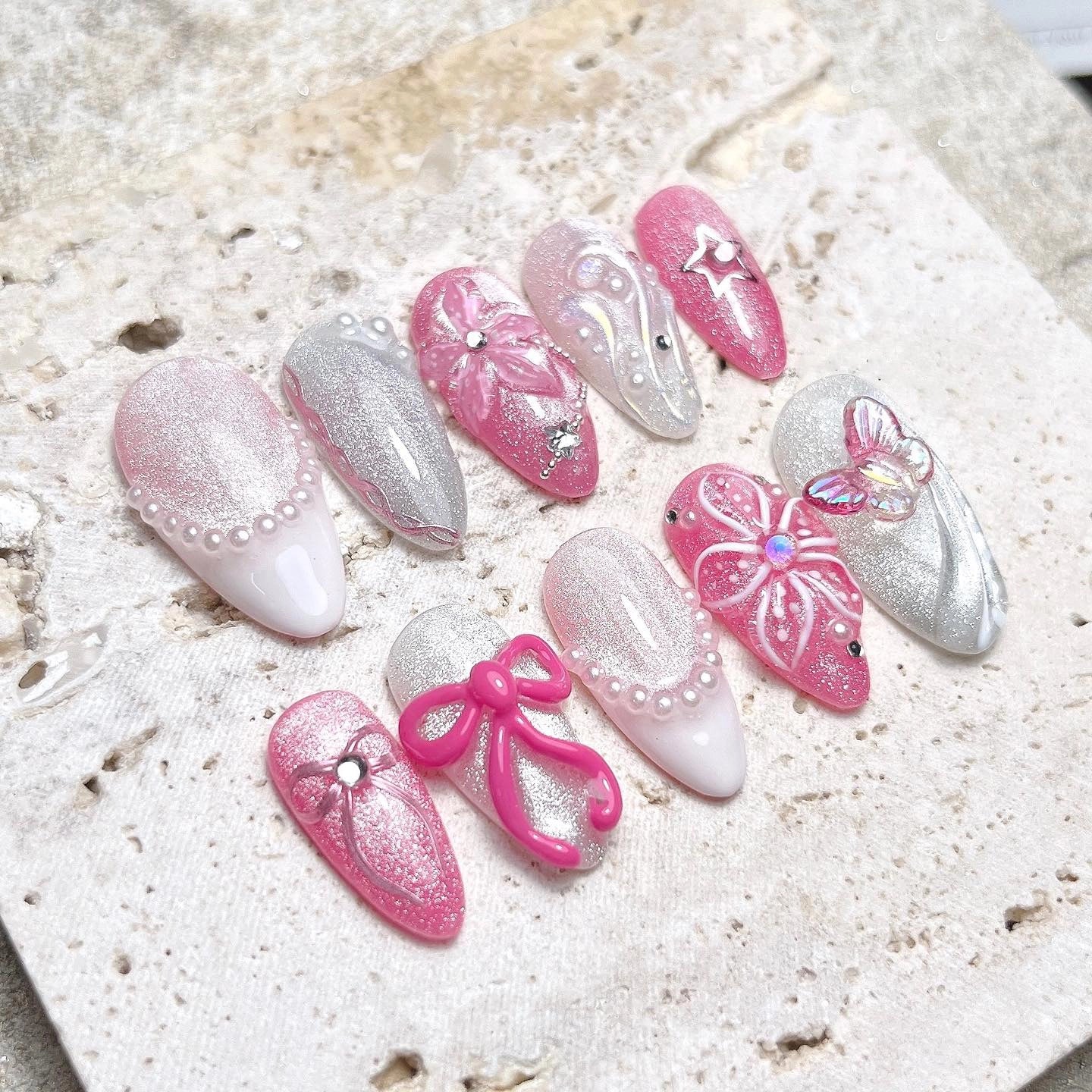 Handmade iridescent pink shimmer press-on nails with 3D flowers, bows, pearls, and butterfly accents.