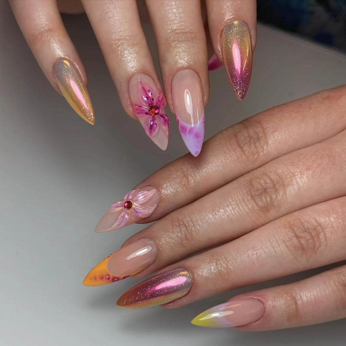 Hand with iridescent sunset chrome pink press-on nails and 3D floral accents