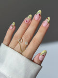 Hand with pink and yellow French tip press-on nails, featuring ladybug and floral vine designs.