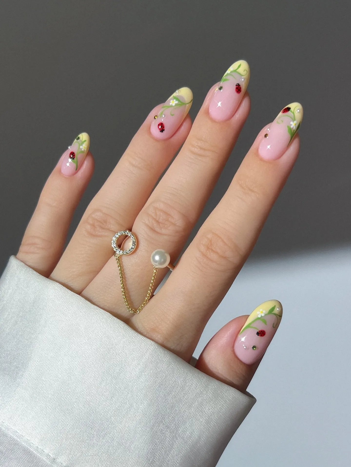 Hand with pink and yellow French tip press-on nails, featuring ladybug and floral vine designs.