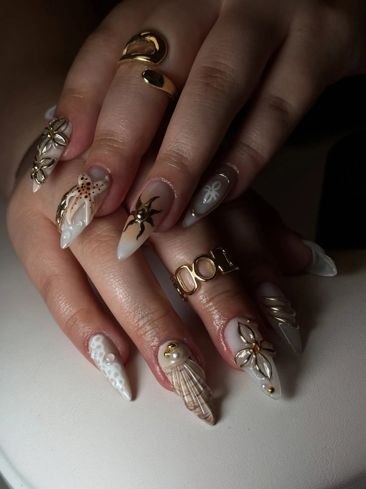 Hand with long press-on nails featuring 3D seashell, starfish, pearl, and gold coastal designs.