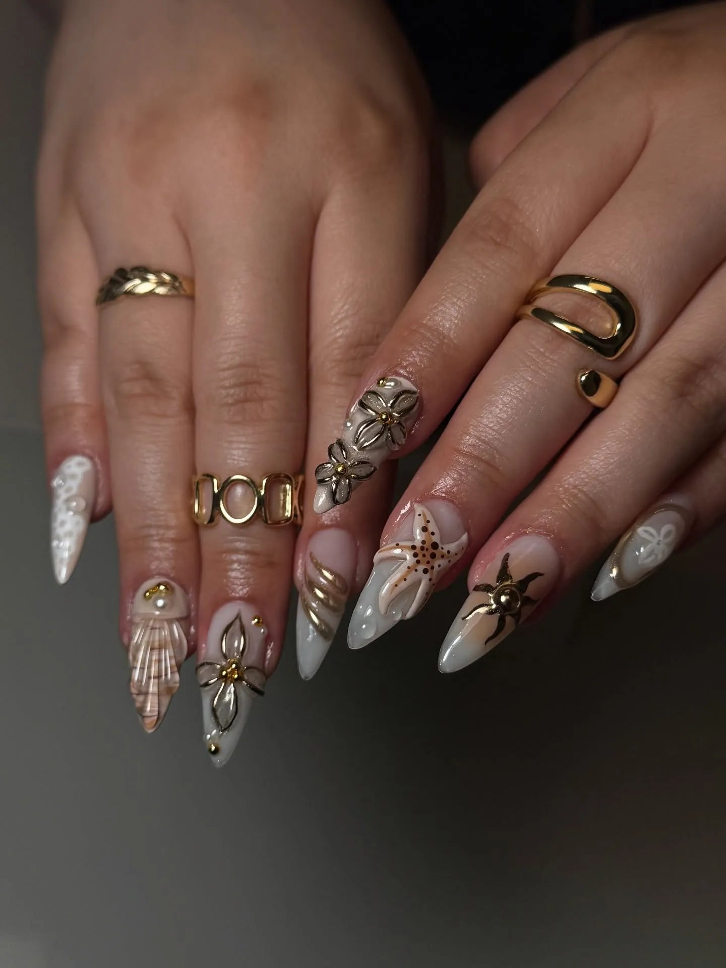 Hand with long stiletto press-on nails featuring 3D seashell, starfish, and pearl coastal designs.