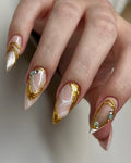 Hand with long stiletto press-on nails featuring gold chrome, marble effect, and gemstone accents