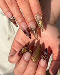 Hand with long stiletto press-on nails in tortoise shell, gold, and gem floral designs.