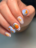 Hand with handmade blue stripe press-on nails featuring citrus fruit and cocktail art.
