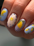Hand with handmade Mediterranean citrus press-on nails featuring lemon and stripe designs.