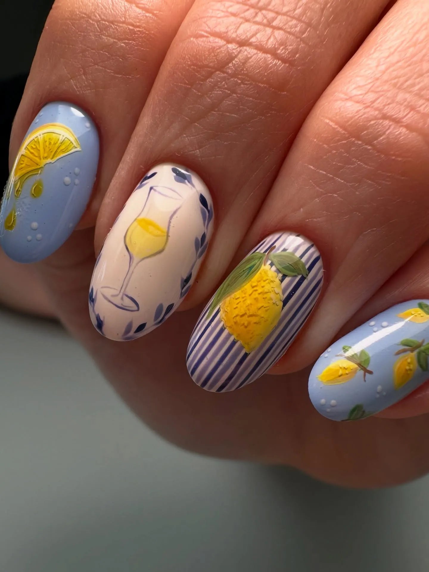 Hand with handmade Mediterranean citrus press-on nails featuring lemon and stripe designs.