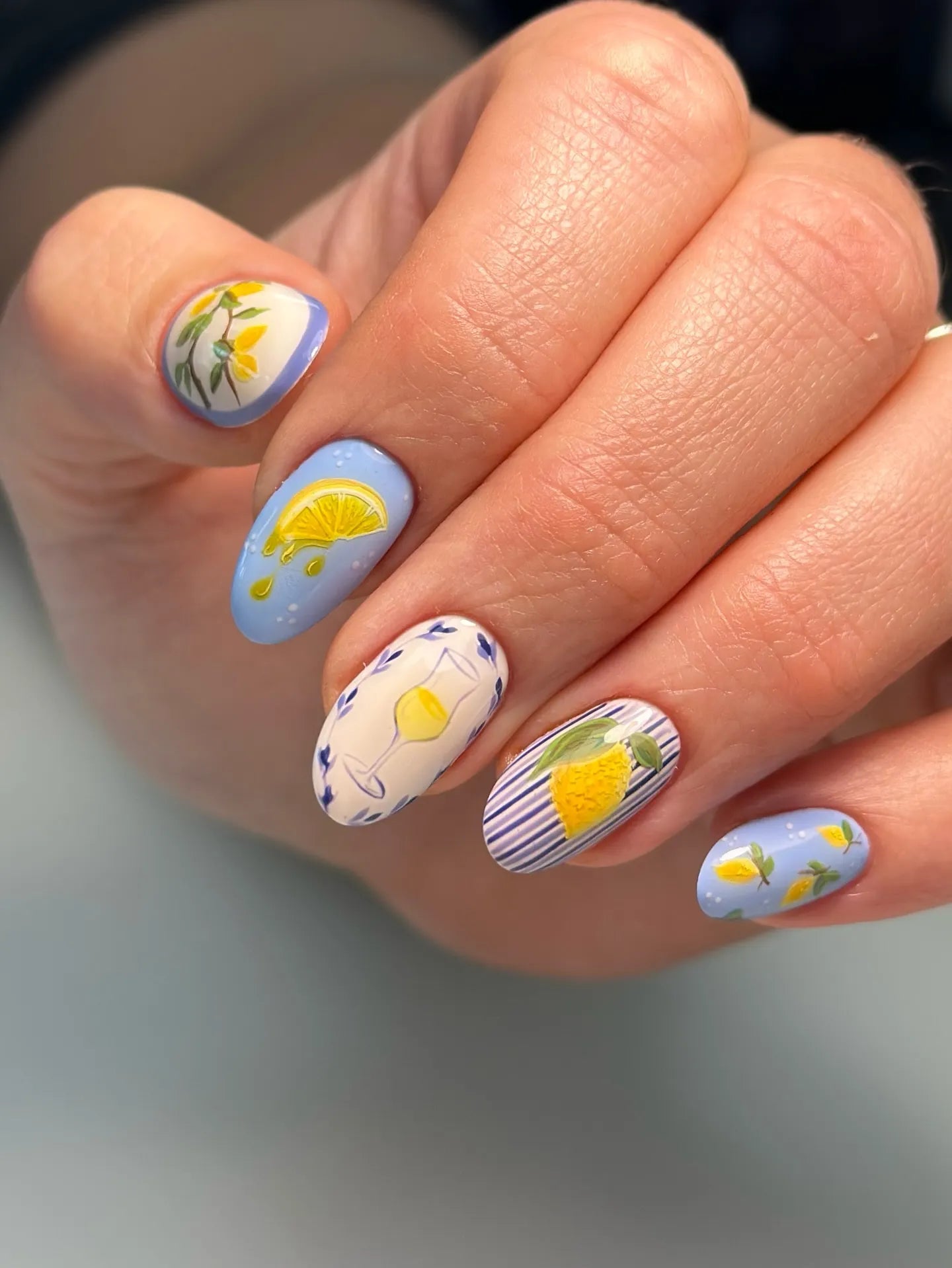 Hand with handmade blue press-on nails featuring citrus fruit, lemon, and summer designs.