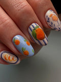 Hand with handmade press-on nails featuring blue stripes and orange citrus fruit art