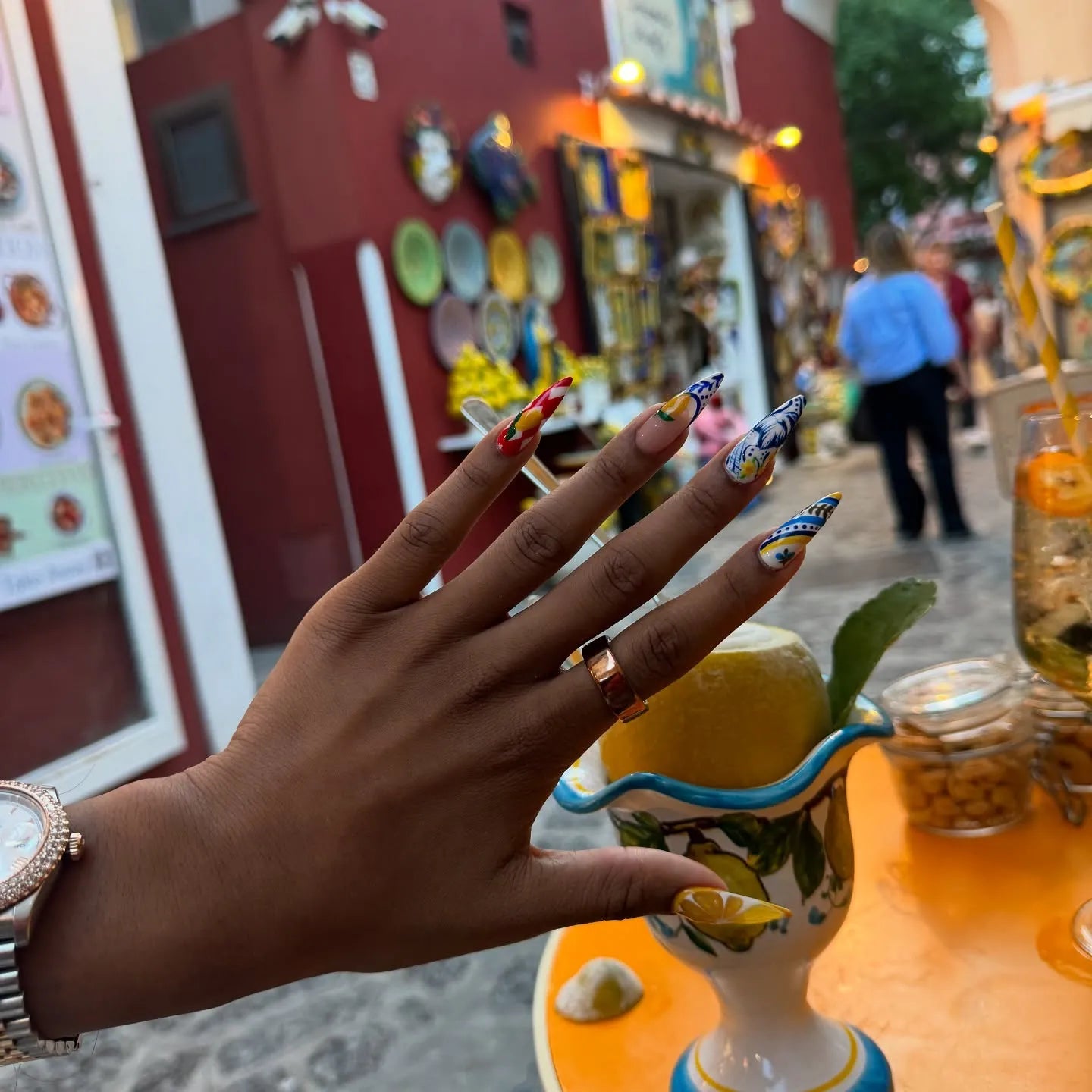 Hand with long Mediterranean lemon blue and white Talavera press-on nails outdoors