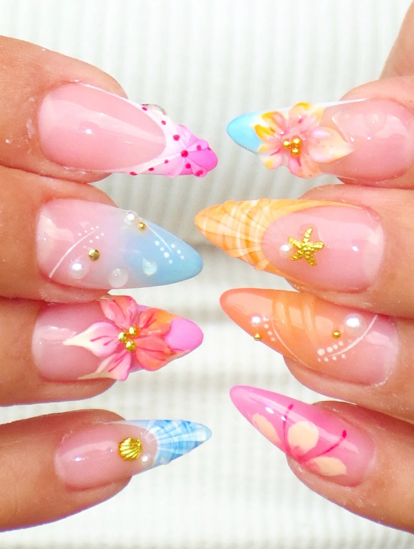 Handmade press-on nails with tropical floral designs, seashell and pearl accents, colorful tips.