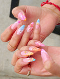 Hand with long press-on nails featuring mermaid shells, tropical flowers, pearls, and pastel colors.