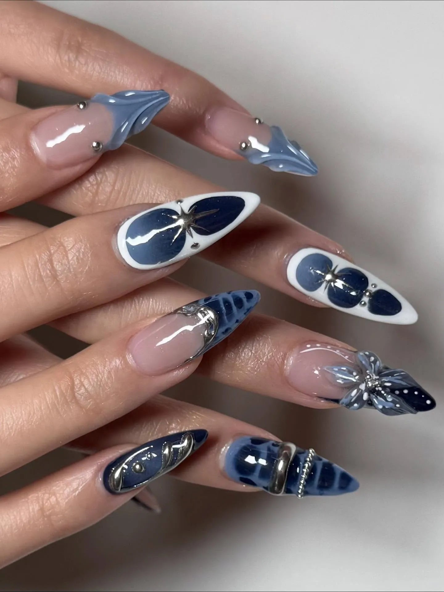 Hand with midnight blue and white 3D floral celestial chrome stiletto press-on nails.