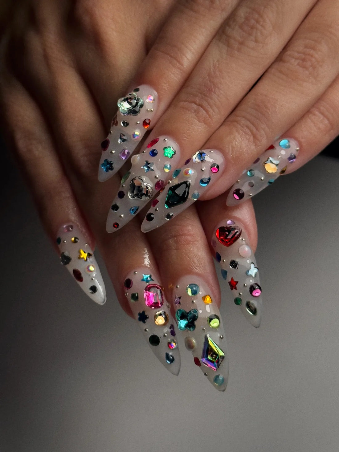 Hand with extra long stiletto press-on nails decorated with colorful 3D gemstones
