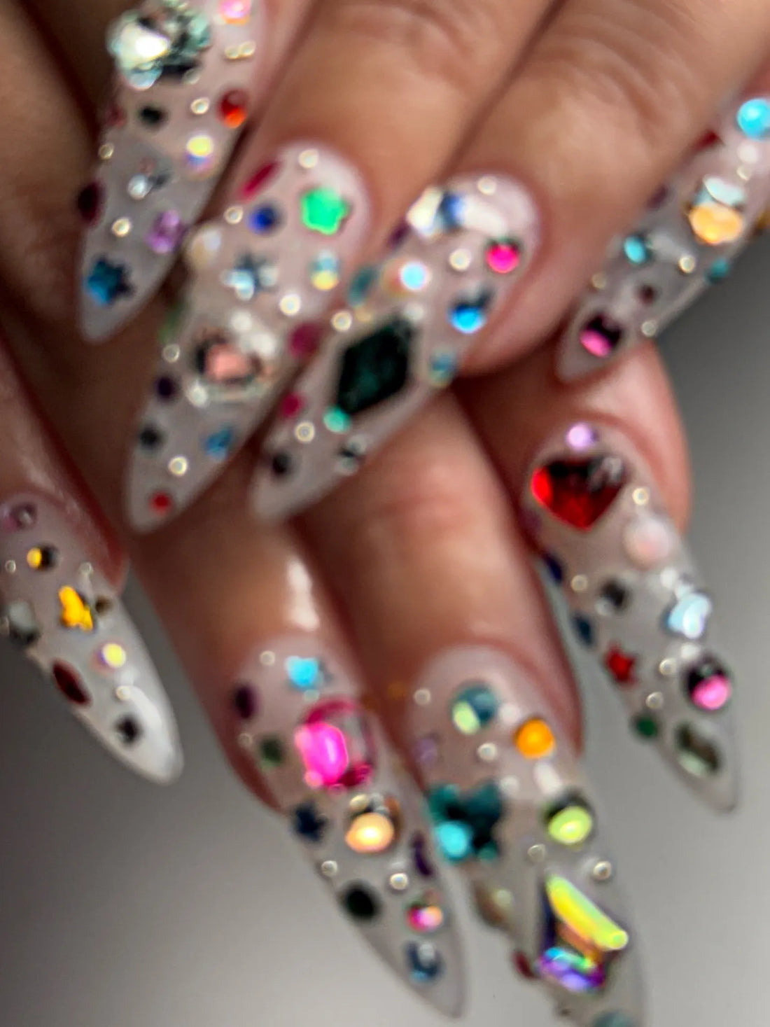 Hand with extra long stiletto press-on nails decorated with colorful 3D gemstones