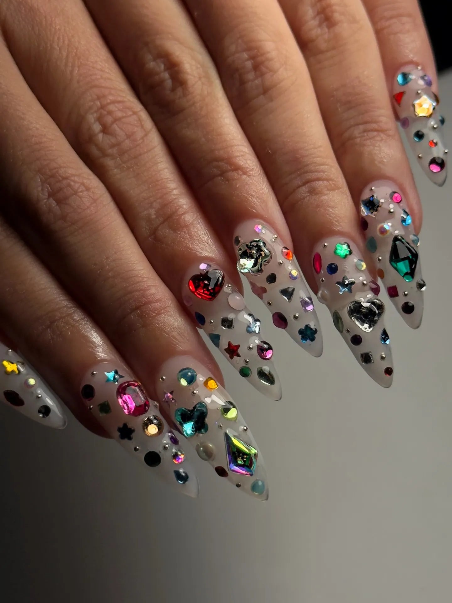 Hand with extra long stiletto press-on nails featuring 3D gemstone and galaxy-inspired designs
