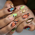 Hand with luxury handmade press-on nails featuring monarch butterfly art, crystals, and metallic accents.